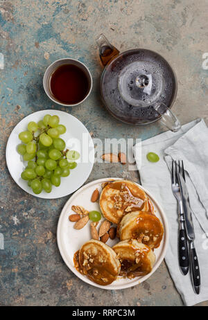 Fastnacht Maslenitsa Butter Woche festival Mahlzeit. Stapel Pfannkuchen Blini mit Karamell mit Nüssen, grüne Trauben, Tee. Nahaufnahme, Ansicht von oben. Konzept auf shrov Stockfoto