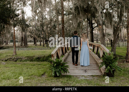 Schöne Brautjungfer Frau im blauen Kleid und Blumenstrauß mit Ihr Datum in einer feierlichen Hochzeit Party Feier Veranstaltung außerhalb im Wald unter Paar Port Stockfoto