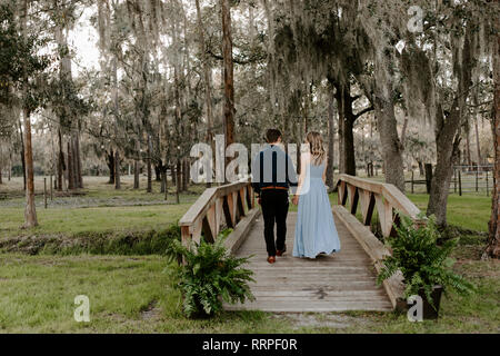 Schöne Brautjungfer Frau im blauen Kleid und Blumenstrauß mit Ihr Datum in einer feierlichen Hochzeit Party Feier Veranstaltung außerhalb im Wald unter Paar Port Stockfoto