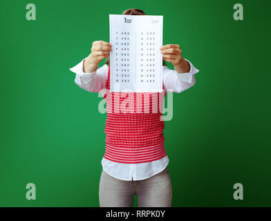 Moderne Student in Grau jeans und Pink ärmelloses Shirt Holding A+ Prüfung Ergebnis vor Gesicht auf grünem Hintergrund. Stockfoto