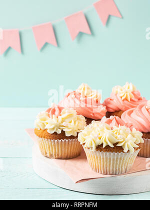 Muffins sind mit dicken weißen und rosa Creme hellblau Hintergrund rosa festliches Flaggen dekoriert. Festliche essen Konzept. Stockfoto