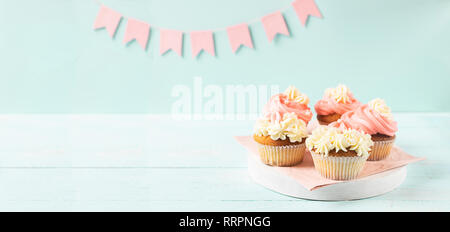Muffins sind mit dicken weißen und rosa Creme auf einem hellblauen Hintergrund mit Rosa festliches Flaggen dekoriert. Stockfoto