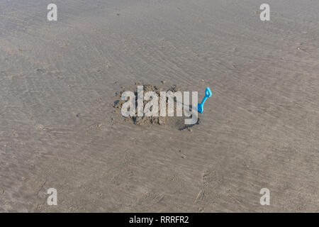Kinder meer Spaten neben einem Loch in feuchten Sand gegraben. Metapher für Strandurlaub, graben Sie ein Loch für sich selbst, schwierigen Situationen, Brexit deal Stockfoto