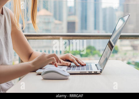 Junge Frau lehrt eine Fremdsprache lernt eine Fremdsprache im Internet auf ihrem Balkon vor dem Hintergrund einer großen Stadt. Online Sprache Stockfoto