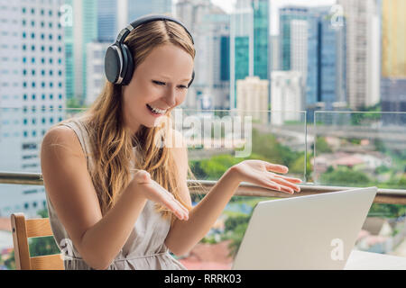 Junge Frau lehrt eine Fremdsprache lernt eine Fremdsprache im Internet auf ihrem Balkon vor dem Hintergrund einer großen Stadt. Online Sprache Stockfoto