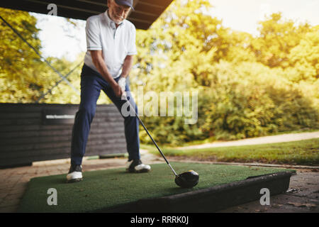 Sportliche älterer Mann üben sein Schwingen mit einem Fahrer an einem golf driving range an einem sonnigen Tag Stockfoto