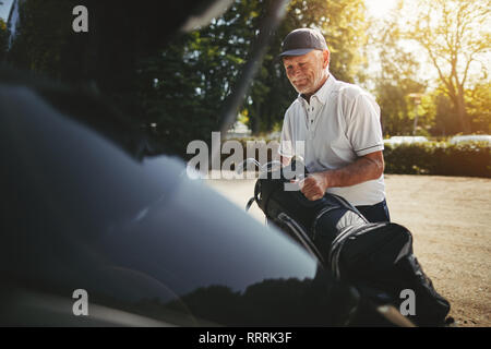 Lächelnd älterer Mann Verpackung sein Golf Tasche in den Kofferraum seines Autos nach dem Spielen Sie eine Runde Golf auf einem sonnigen Nachmittag Stockfoto