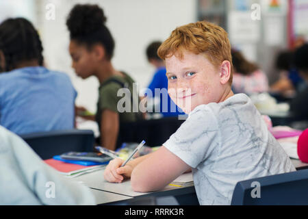 Porträt Lächeln, zuversichtlich Junior high school junge Studenten studieren an Schreibtisch im Klassenzimmer Stockfoto
