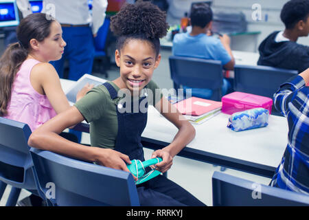 Porträt Lächeln, zuversichtlich Junior high school girl Student mit Kopfhörern am Schreibtisch im Klassenzimmer Stockfoto