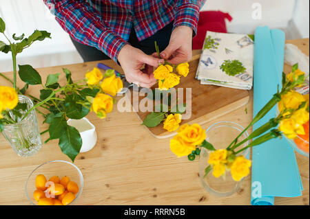 Eine Frau florist macht einen Blumenstrauß. Auf dem Tisch liegen Blumen Rosen. Mädchen mit einer Schere schneidet die Rose. Stockfoto