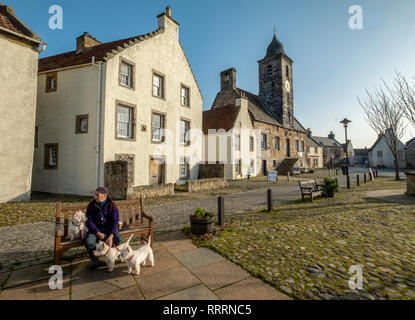 Ein Mann mit drei West Highland Terrier sitzen auf einer Bank in dem historischen Dorf folgende Sehenswürdigkeiten: Culross, Fife, Schottland. Stockfoto