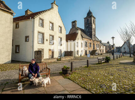 Ein Mann mit drei West Highland Terrier sitzen auf einer Bank in dem historischen Dorf folgende Sehenswürdigkeiten: Culross, Fife, Schottland. Stockfoto