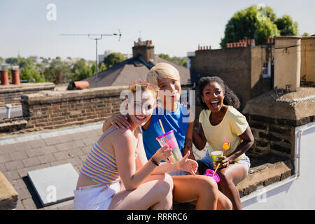 Portrait glückliche, selbstbewusste junge Frauen Freunde trinken auf sonnigen Sommer Dachterrasse Stockfoto