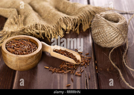 Zusammensetzung der Menge ganze rohe rote Reis mit Houten auf braunem Holz Stockfoto