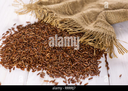 Menge ganze rohe rote Reis auf Jute-stoff auf weißem Holz Stockfoto