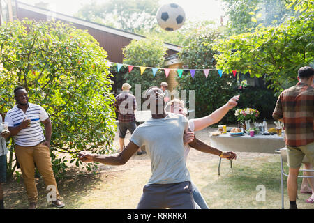 Männliche Freunde Fußball spielen, genießen Hinterhof Sommer Grill Stockfoto