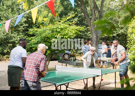 Männliche Freunde spielen Ping pong im sonnigen Hinterhof Stockfoto