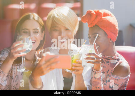 Junge Frauen, die Freunde trinken Cocktails und unter selfie mit smart phone in Sunny Bar Stockfoto