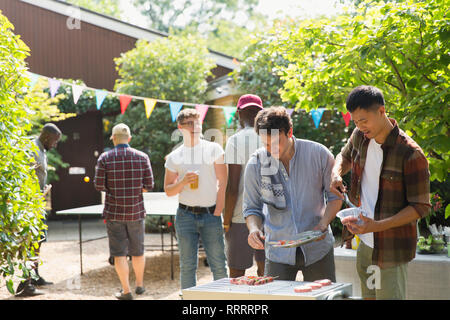 Männliche Freunde genießen Grill im sonnigen Hinterhof Stockfoto
