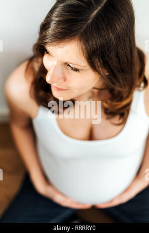 Hohe Betrachtungswinkel der schwangeren Frau in weißem Hemd ihr Holding Bauch Stockfoto