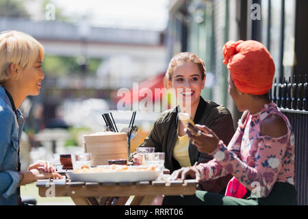 Junge Frauen, die Freunde genießen dim sum Mittagessen im sonnigen Straßencafé Stockfoto