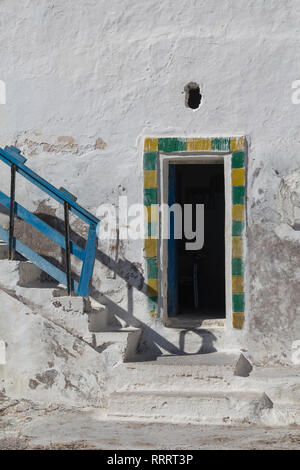 Weiß verwitterte Wand eines Hauses mit geöffneten Tür, mit Gelb und Grün umrahmt. Treppen auf der linken Seite, die mit einem blauen Geländer. Sidi Kaouki, Marokko. Stockfoto