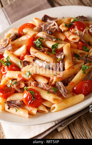 Penne Pasta mit gezogen, Schweinefleisch, Käse, Tomatensauce close-up auf einem Teller auf den Tisch. Vertikale Stockfoto