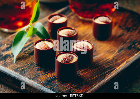 Glas transparent Teekanne und zwei Glas Tassen mit schwarzem Kaffee mit Schokolade Süßigkeiten Sortiment onwooden cutboard Stockfoto