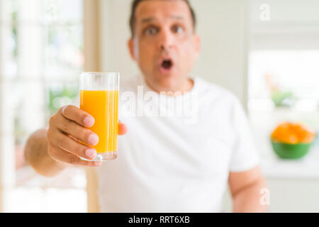 Mittleres Alter Mann trinkt ein Glas Orangensaft zu Hause Angst im Schlag mit einer Überraschung konfrontiert, ängstlich und aufgeregt mit Angst Ausdruck Stockfoto