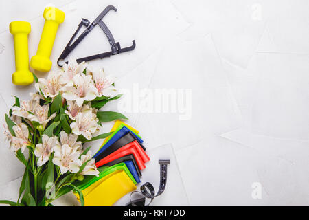 Ansicht von oben Bild von Kurzhanteln, bunte elastische Gummi Expander, Bremssättel und Maßband auf einem weißen strukturierten Hintergrund. Gesunder Lebensstil, Fitnessraum und nicht Stockfoto