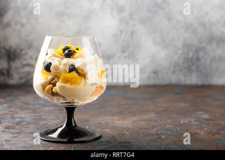 Gesunde hausgemachte layered Dessert trifle mit Orange, Heidelbeere, Keksen, Joghurt und Müsli in einer Brille. Für text Stockfoto