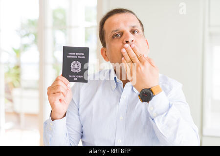 Mittleres Alter Mann Holding holding Passport von Italien decken den Mund mit der Hand mit Schande für den Fehler, den Ausdruck von Angst erschüttert, die in der Stille Angst, geheime c Stockfoto