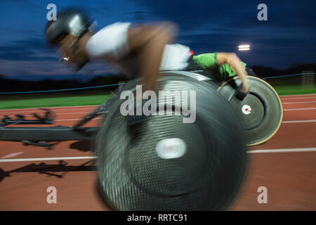 Querschnittsgelähmte Sportler Beschleunigung zusammen Sport Track im Rollstuhl Rennen bei Nacht Stockfoto