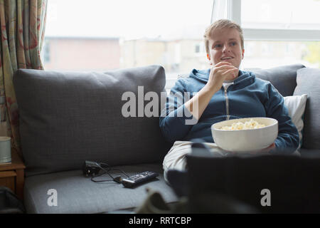 Junge Frau Essen Popcorn auf sofa Stockfoto