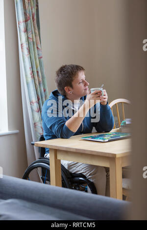 Nachdenkliche junge Frau im Rollstuhl Tee trinken am Esstisch Stockfoto