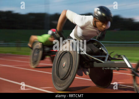 Bestimmt jungen männlichen querschnittsgelähmten Athlet Beschleunigung zusammen Sport Track im Rollstuhl Rennen Stockfoto