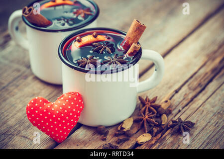 Glühwein im Becher, rote Herzen und Gewürz auf alten Holztisch. Im Retrostil. Stockfoto