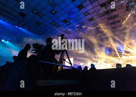 Fernsehen von einem Kameramann bei einem Konzert. Kamera mit dem Operator ist auf der Plattform. Silhouetten auf dem Hintergrund der bunte Strahl Stockfoto