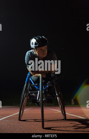 Entschlossene junge weibliche paraplegic Athlet Training für Rollstuhl Rennen am Sportplatz in der Nacht Stockfoto