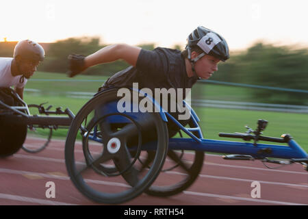 Entschlossene junge weibliche paraplegic Athlet Beschleunigung zusammen Sport Track im Rollstuhl Rennen Stockfoto