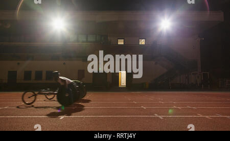 Männlichen querschnittsgelähmten Athlet Training für Rollstuhl Rennen am Sportplatz in der Nacht Stockfoto