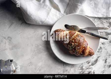 Ein Croissant auf einem weissen Teller, mit einer Gabel und ein Messer, ein weißes Handtuch Stockfoto