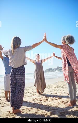 Gruppe Hand in Hand im Kreis an sonnigen Strand während Yoga Retreat Stockfoto
