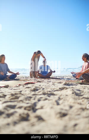 Heitere Menschen meditieren auf sonnigen Strand während Yoga Retreat Stockfoto