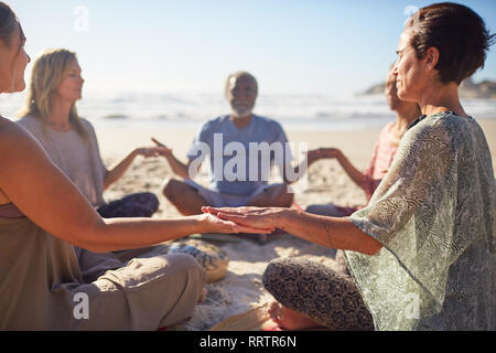 Heitere Menschen meditieren im Kreis an sonnigen Strand während Yoga Retreat Stockfoto