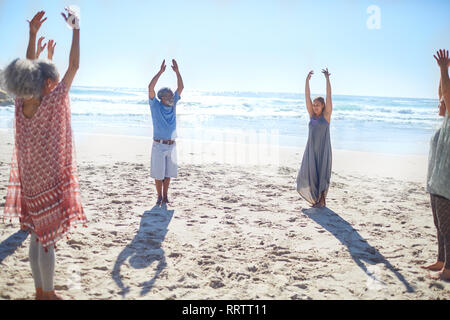 Gruppe stehend mit Waffen im Kreis auf sonnigen Strand während Yoga Retreat Stockfoto