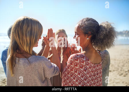 Frauen Freunde mit gefalteten Händen in Kreis an sonnigen Strand während Yoga Retreat Stockfoto