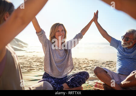 Gerne Freunde Hand in Hand im Kreis an sonnigen Strand während Yoga Retreat Stockfoto