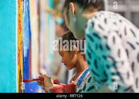 Lehrer und Schüler der Grundschule Mädchen Gemälde an der Wand Stockfoto