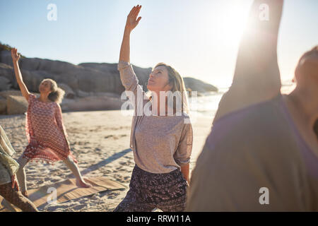 Heitere Frau üben Reverse warrior Pose an sonnigen Strand während Yoga Retreat Stockfoto